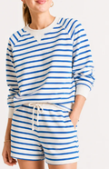 A woman wearing a matching blue and white striped lounge set, featuring a long-sleeve sweatshirt and shorts with a white drawstring, against a plain light background.