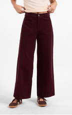 A person wearing high-waisted, wide-leg corduroy pants in deep burgundy, styled with a cream t-shirt and brown flat sandals against a plain white studio background.