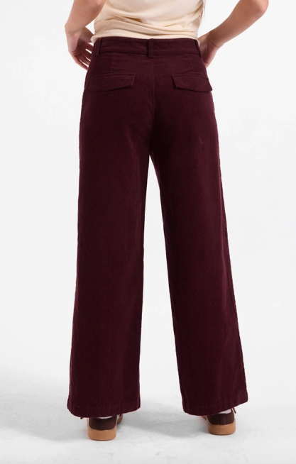A person shown from the back wearing burgundy wide-leg corduroy pants, a light beige top, and brown shoes against a plain white studio background.