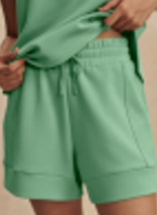 A close-up of a person wearing mint green drawstring shorts, pulling up a matching mint green top with both hands.