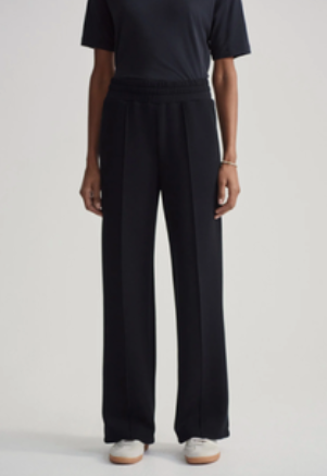 A model wearing black wide-leg trousers with a matching black short-sleeve top, paired with white sneakers, against a plain light gray background.