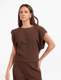 A woman modeling a brown ribbed knit two-piece set featuring a short-sleeve cropped top with draped sleeves and matching ribbed trousers, shot against a plain white studio background.